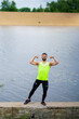 © Georgii - Happy athletic young guy in stylish sportswear posing showing muscles outdoor near water