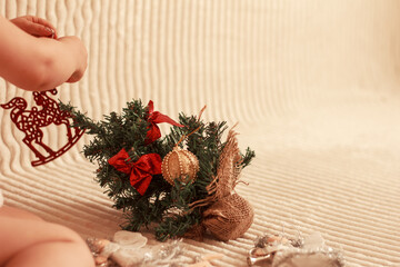 Little Christmas tree lying on beige background, christmas decorations and little hands of a child sitting and decorating Christmas tree. Merry Christmas year concept. Place for text o design, selecti