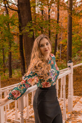 Wall Mural - Joyful teenager stands leaning against a white railing, a young blonde with a kind look, in a colored shirt, positive emotions on the background of innocent autumn steps standing bright blue eyes