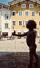Bad Tölz, Bavaria, Germany: Silhouette Of Brunnenknabe (Young Boy Fountain) By Fernando De La Jara (bronze And Granite) On Marktstrasse. Child With Flower Crown Holds A Bird. 