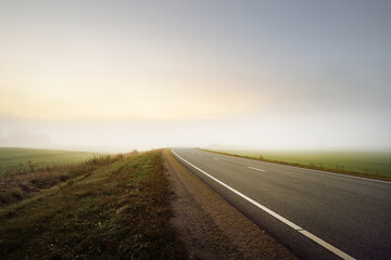 Wall Mural - Panoramic view of the empty highway through the fields and forest in a fog at sunrise. Europe. Transportation, logistics, travel, road trip, freedom, driving. Rural scene