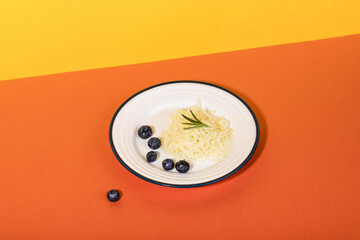 Grated cheese with rosemary and blueberries on a plate on an orange and yellow table