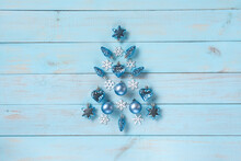 Christmas Light Blue Background. Festive Decoration With Blue And Silver Baubles, Hearts, Snowflakes, Stars, Cones In Christmas Tree Shape Arranged On Rustic Pastel Blue Wooden Table, Top View.