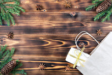 Christmas Box With A Gift In A Paper Bag On A Wooden Background With Spruce Branches, Anise Heres And Cones