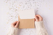 © ActionGP - Top above close up overhead view photo of female hands holding kraft paper envelope with mock up copy space card inside over shiny golden background table