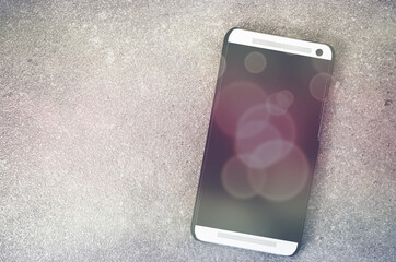 Wall Mural - Top view of the smartphone on a rough stone background with copy space and bokeh background