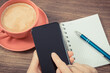 Hand of woman with mobile phone, coffee with milk and notepad for notes. Work or relaxation