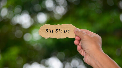 Wall Mural - Big Steps Text On Hands Holding Torn Paper With Blurred Dark Background