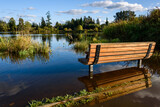 Fototapeta Pomosty - Wooden bench on the flooded shore of Larson Lake, reflections of blue sky and clouds
