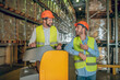 © zinkevych - Warehouse workers in orange helmets standing near shelves and talking