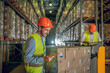 © zinkevych - Male warehouse workers in helmets standing near cardboard boxes