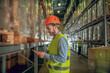 © zinkevych - Male warehouse worker in helmet standing near containers and holding a tablet