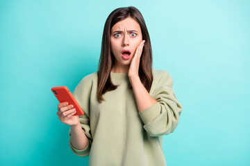 Poster - Photo portrait of confused scared woman with open mouth holding phone in one hand isolated on vivid turquoise colored background