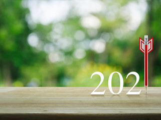 Red pencil in the shape of a dart with 2021 white text on wooden table over blur green tree in park, Business strategy happy new year 2021 cover concept