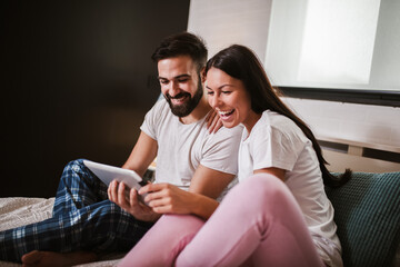 Wall Mural - Smiling relaxed young couple using digital tablet in bed at home
