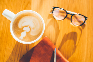 Сup of coffee write pen in a notebook on a wooden table.