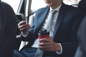 Wall Mural - Businessman using smartphone inside car and drinking morning coffee while going to workplace