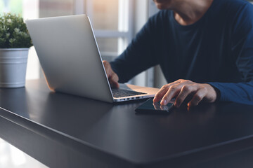 Wall Mural - Casual man working on laptop computer and using mobile smart phone on office table at home