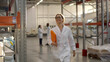 Young woman engineer in white coat walking in large factory warehouse