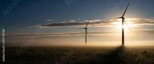 Canvas Print Two wind turbines in the early morning fog at sunrise in the English countryside
