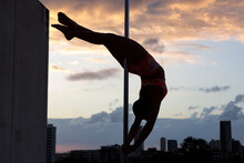 Feminine Middle Eastern Pole Dancer, Holding A Pose On A Pole Set Outdoors. Silhouette Shot With Tel Aviv Buildings In The Far Background.