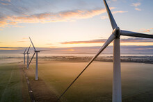 Aerial View Of Three Wind Turbines In The Early Morning Fog At Sunrise In The English Countryside