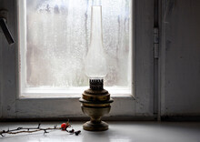 Soft Focus On Vintage Oil Lamp On The Windowsill With Twig In Blurred Rainy Window Background. Close Up