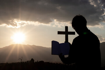 Silhouette of human kneeling down praying and holding christian cross for worshipping God at sunset background. Christian, Christianity, Religion copy space background.