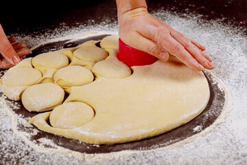 Woman cuts out dough with round mold for making buns, dounuts.