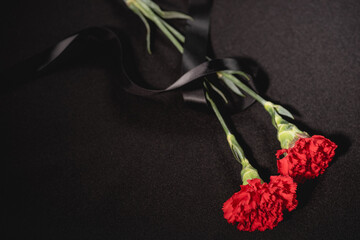 Wall Mural - top view of two red carnation flowers with ribbon on black , funeral concept