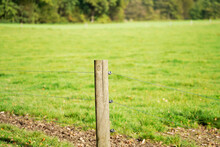 Closeup Of A Short Wooden Pole With Metal Wires Connected To It To Make A Fence Near The Field