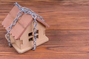 House in chains on wood background. Protection, security, alarm concept