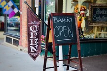 Street View In The Small Town Of Canandaigua, New York. American Traditional Displays And Decorations On Sidewalks. Bakery Shop With “Open” Sign 