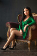 © Northern life - Sexy brunette woman in short green dress posing on the armchair dark interior .