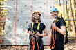 Portrait of a young couple well equipped in safety gear standing together in front on the climbing wall at amusement park