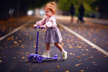 Cute Redhead Baby Girl Scootering In Autumn Park