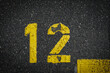 © YK - Grey asphalt road, yellow painted number twelve on grey street, yellow lines like a corner on the road, space for text