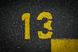 © YK - Grey asphalt road, yellow painted number thirteen on grey street, yellow lines like a corner on the road, space for text