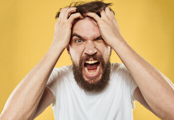 A man with a beard gestures with his hands near his face on a yellow background