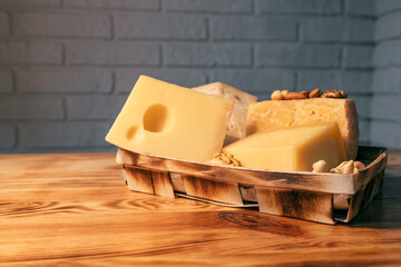 A variety of aged cheeses in a substrate on a wooden table against a brick wall