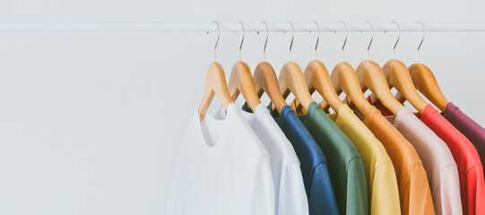 close up collection of colorful t-shirts hanging on wooden clothes hanger in closet or clothing rack over white background, copy space
