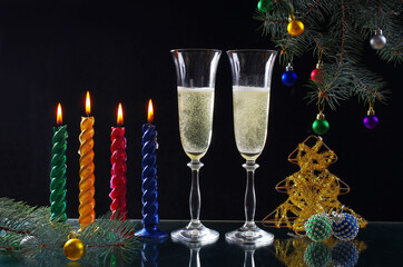 Canvas Print - Four burning candles, two glasses of champagne, Christmas tree branch on a black background