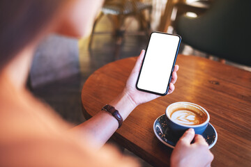 Mockup image of a woman holding mobile phone with blank white desktop screen while drinking coffee