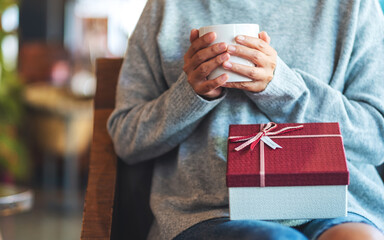 Wall Mural - Closeup image of a woman holding a gift box while drinking coffee