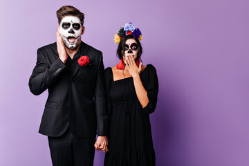 Close-up portrait of goggle man in black jacket with rose on his chest and woman with flowers in dark hair