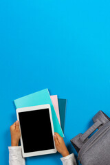 Wall Mural - Kid hands with tablet computer, notebooks, books and gray backpack over light sky blue background