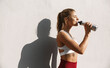 © Liubov Levytska - Satisfied female runner drinking water and smiling after workout. Woman athlete taking break while jogging outdoors, standing by concrete wall