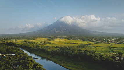 Hillside river at erupt volcano with green grass shore at Philippines countryside aerial. Fields, valley, meadows of nobody nature landscape. Cinematic scenic of Mayon mount erupt at mist haze