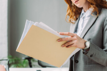 Wall Mural - Cropped view of businesswoman leafing through paper sheets in folder with blurred workplace 