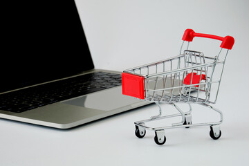 Red color mini shopping cart on desk with laptop on white background. Shopping online concept.